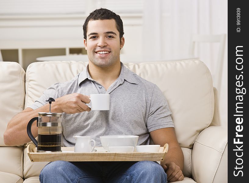 An attractive young man eating from a breakfast tray.  He has a coffee cup raised, and is smiling directly at the camera.  Horizontally framed photo. An attractive young man eating from a breakfast tray.  He has a coffee cup raised, and is smiling directly at the camera.  Horizontally framed photo.