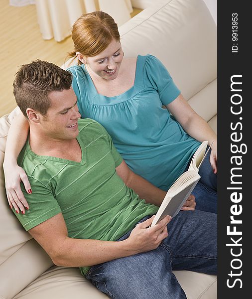 An attractive young couple seated on a couch together and reading from a book.  They are smiling. Vertically framed shot. An attractive young couple seated on a couch together and reading from a book.  They are smiling. Vertically framed shot.