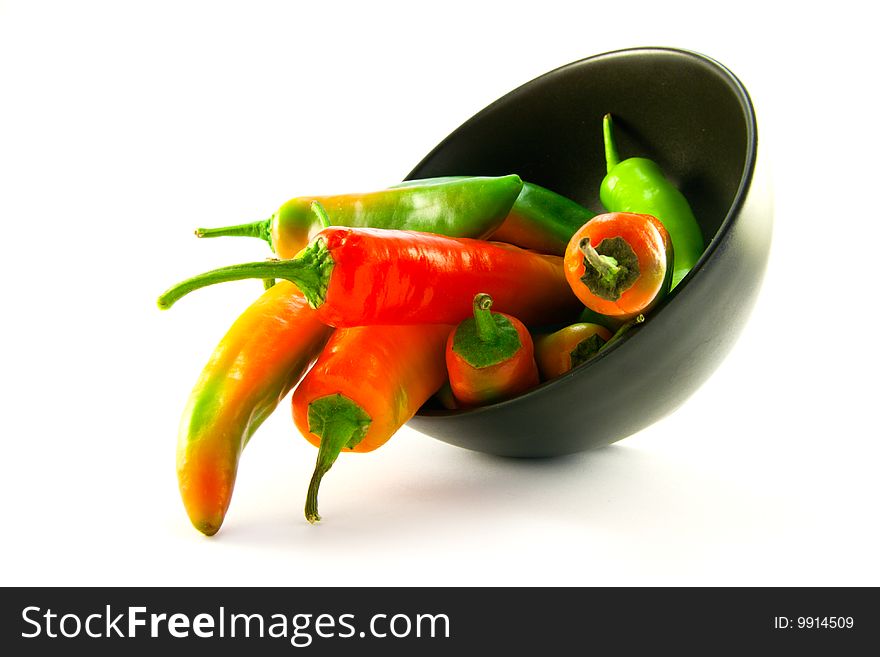 Mixed red and green chillis spilling out of a black bowl with clipping path on a white background