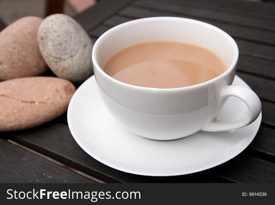 Outdoor cup of tea in a white cup and saucer with stones on a wooden background