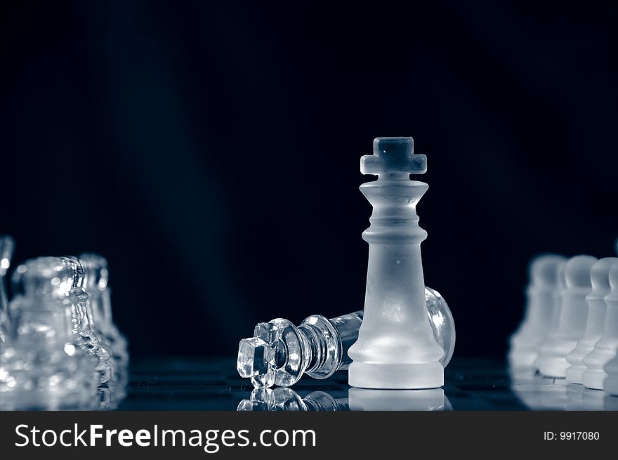 Checkmate with glass king lying on chessboard against black background. Checkmate with glass king lying on chessboard against black background