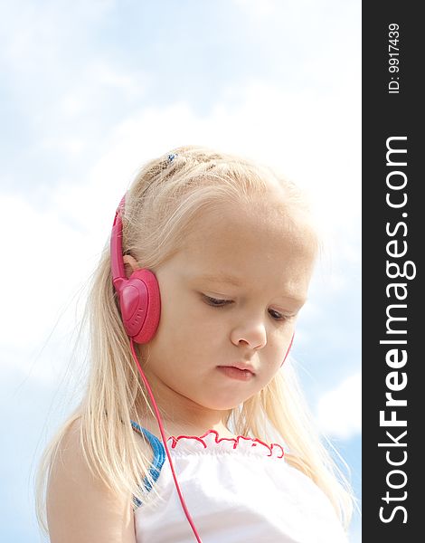 Little blonde girl with closed eyes in red earphones listens mp3 player music outdoor. Little blonde girl with closed eyes in red earphones listens mp3 player music outdoor