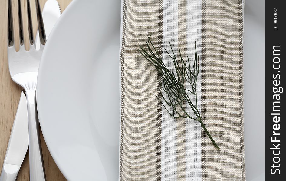 Serving of white plates, forks, knives, cloth napkins with a sprig of dill. Serving of white plates, forks, knives, cloth napkins with a sprig of dill
