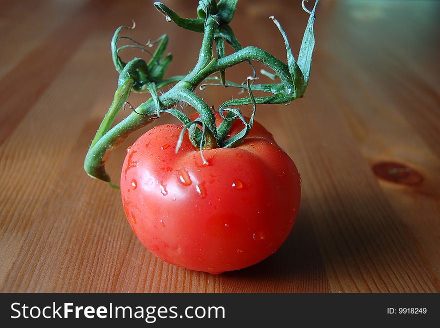 1 red tomato on vine, set on wooden table.