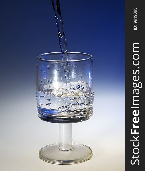 A glass with pouring water on a blue background. A glass with pouring water on a blue background