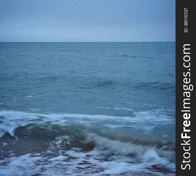 A view of the sea with waves hitting ashore at dusk.