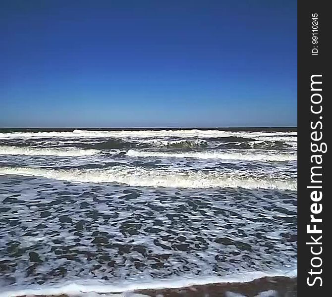 Ocean waves crash on the shore on a sunny day.