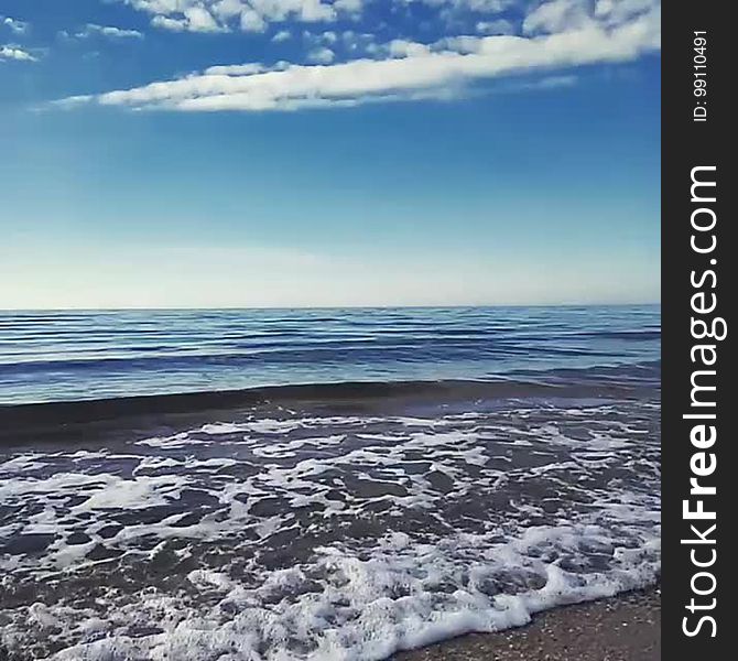 Scenic view of waves breaking on a beach with blue sky and cloudscape background.