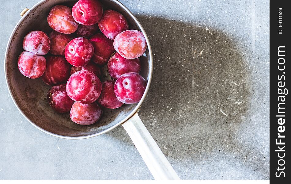 Plums of different varieties in an old metal colander on gray concrete background. Top view. Agriculture, Gardening, Harvest Concept. Plums of different varieties in an old metal colander on gray concrete background. Top view. Agriculture, Gardening, Harvest Concept.