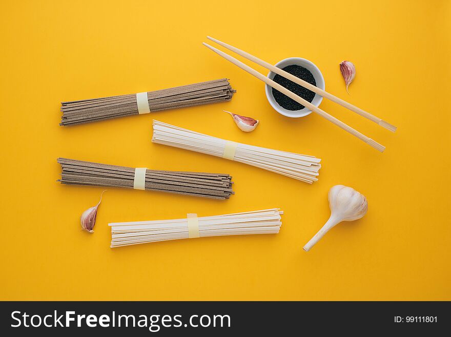 Asian noodles udon and soba, garlic, chopsticks, black sesame in a bowl on a bright yellow background. Minimalism. Flat lay.