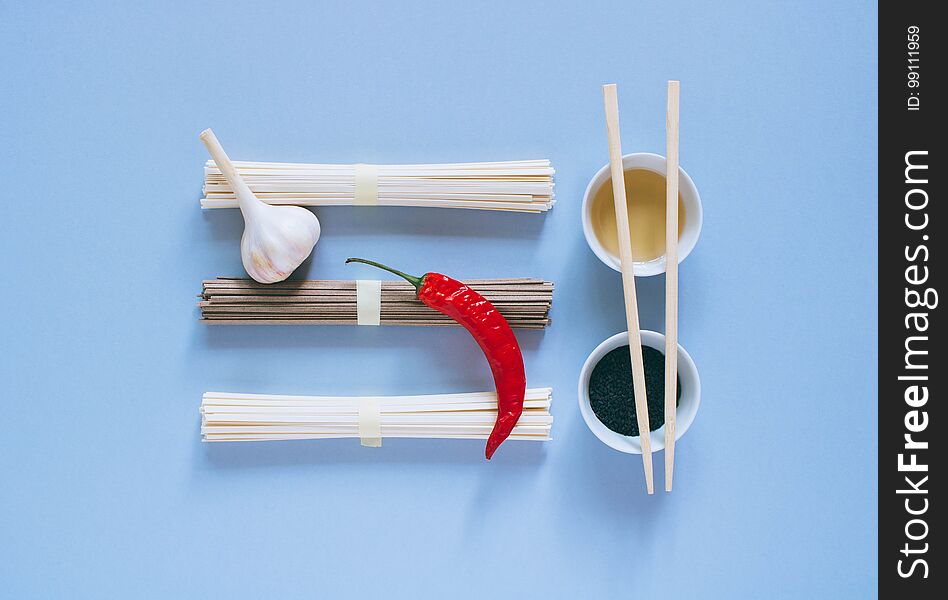 Asian noodles udon and soba, red chili, garlic, chopsticks, black sesame and rice vinegar in bowls on a bright blue background. Minimalism. Flat lay. Asian noodles udon and soba, red chili, garlic, chopsticks, black sesame and rice vinegar in bowls on a bright blue background. Minimalism. Flat lay.
