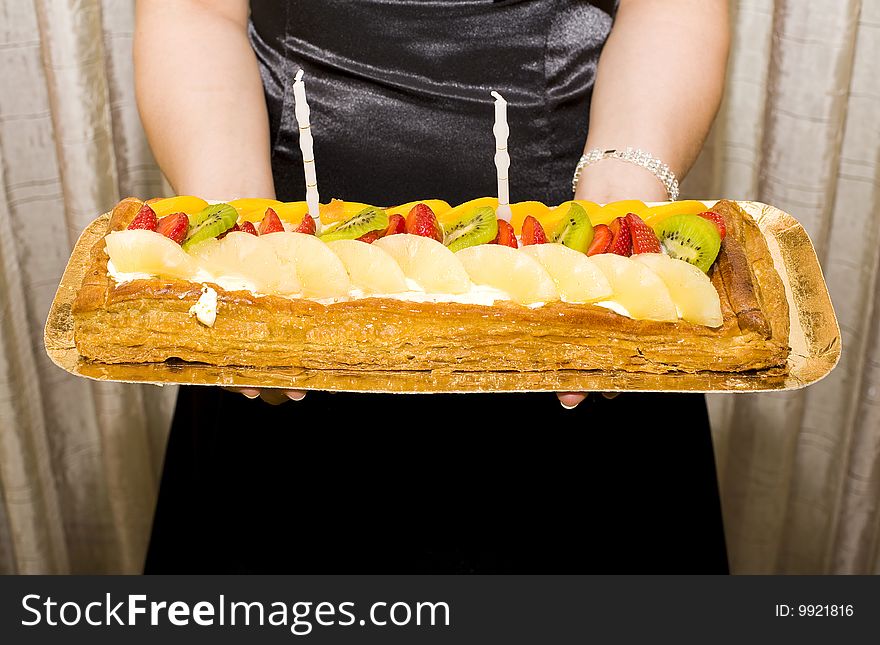 A birthday cake with candles and strawberries and pineapple and kiwi