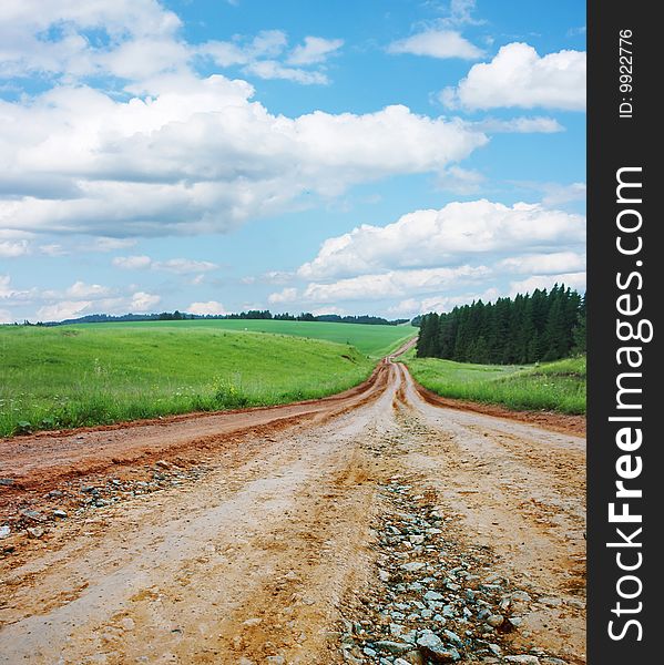 Rural road with gravel with green lawn and blue sky with clouds