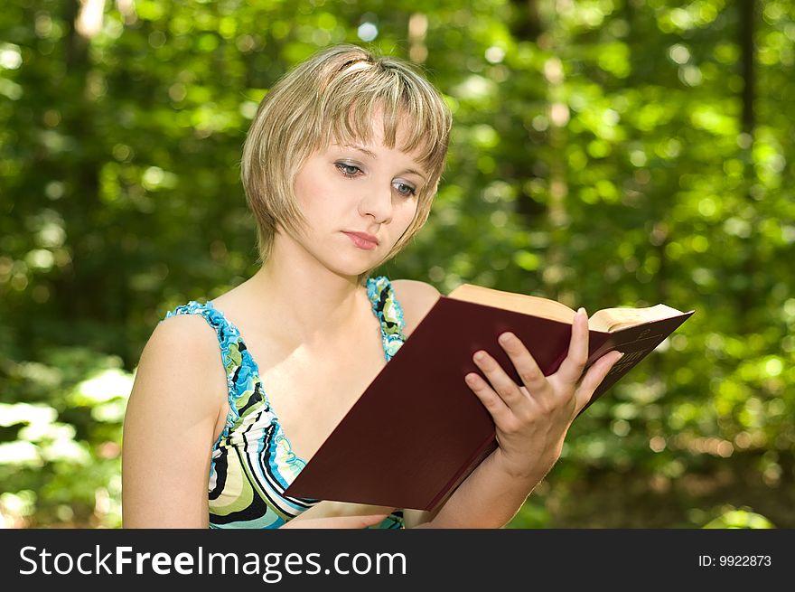 Beautiful student girl reading book in the park