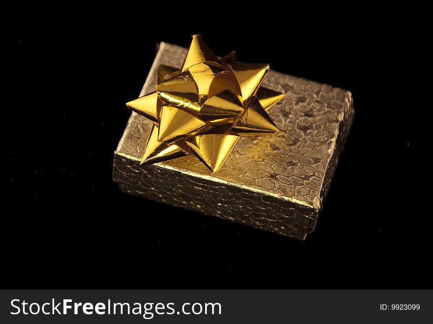 A small textured silver box with a gold bow on a flat black surface. A small textured silver box with a gold bow on a flat black surface