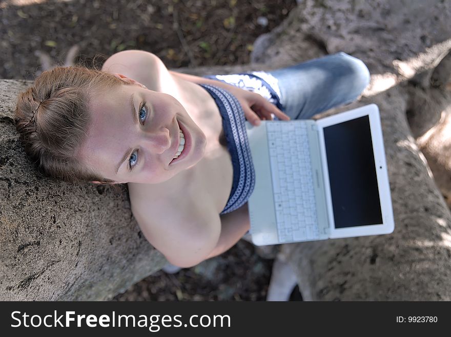 Beautiful young girl working with laptop in tree, photographed from above