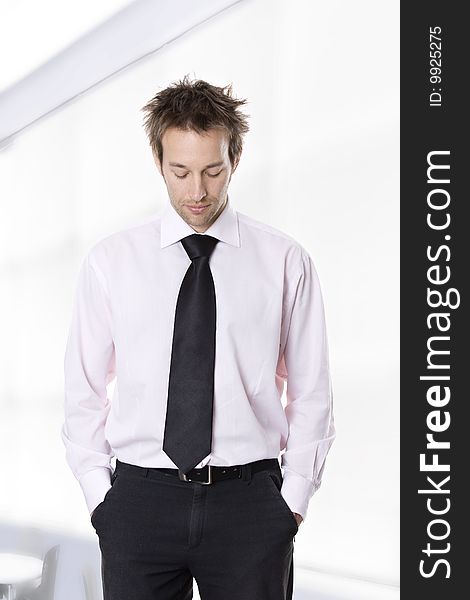 Businessman standing with hands in pocket, looking down.