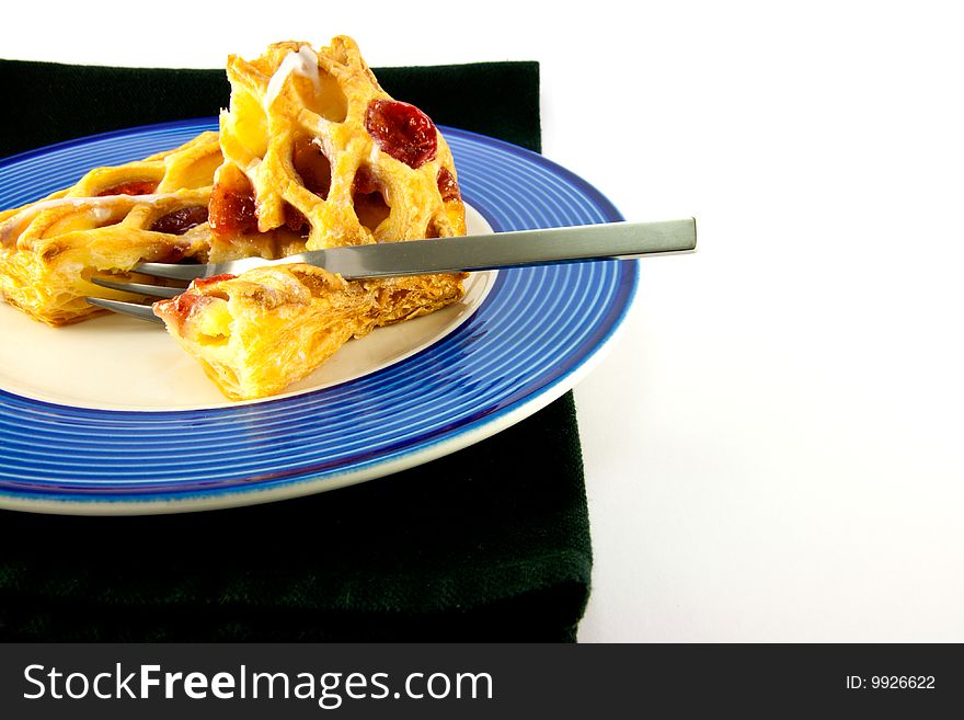 Raspberry and custard danish on a blue and white plate with a fork and black napkin on a white background. Raspberry and custard danish on a blue and white plate with a fork and black napkin on a white background