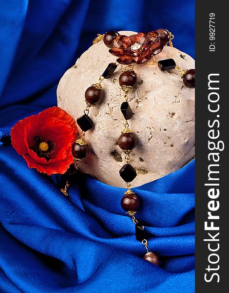 Necklace, flower and stone on a blue textile. Vertical