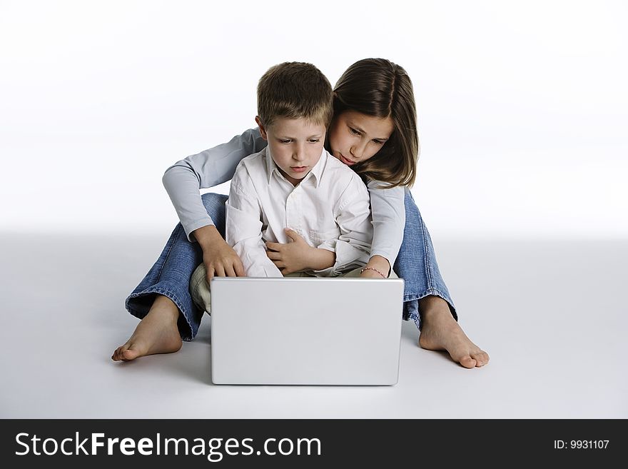 Studio shot on white background of cute boy and girl sitting together with a laptop computer in front of them while girl is pointing the screen. Studio shot on white background of cute boy and girl sitting together with a laptop computer in front of them while girl is pointing the screen