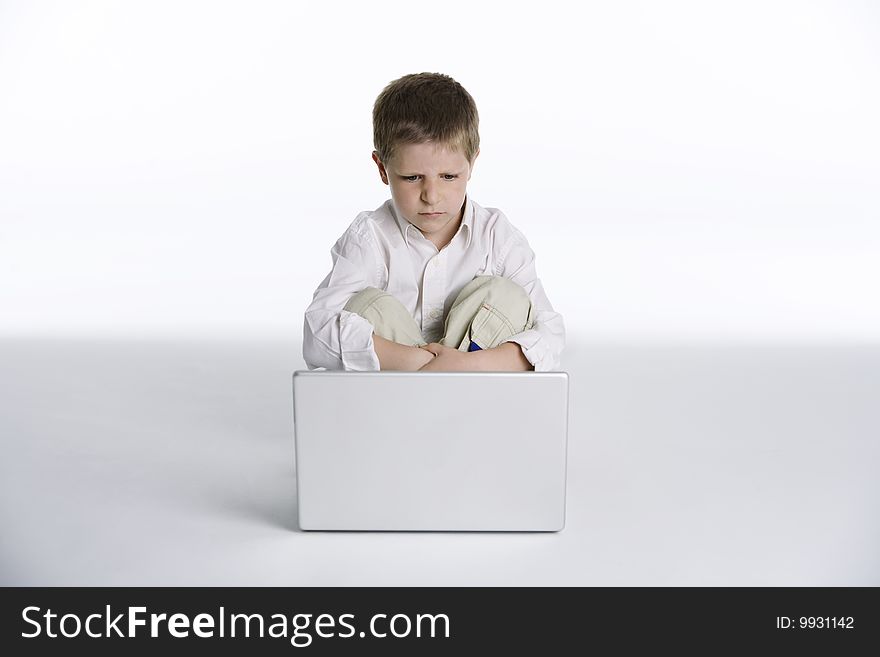 Studio portrait on white background of a cute boy sitting with a disappointed expression while looking at a laptop computer screen. Studio portrait on white background of a cute boy sitting with a disappointed expression while looking at a laptop computer screen