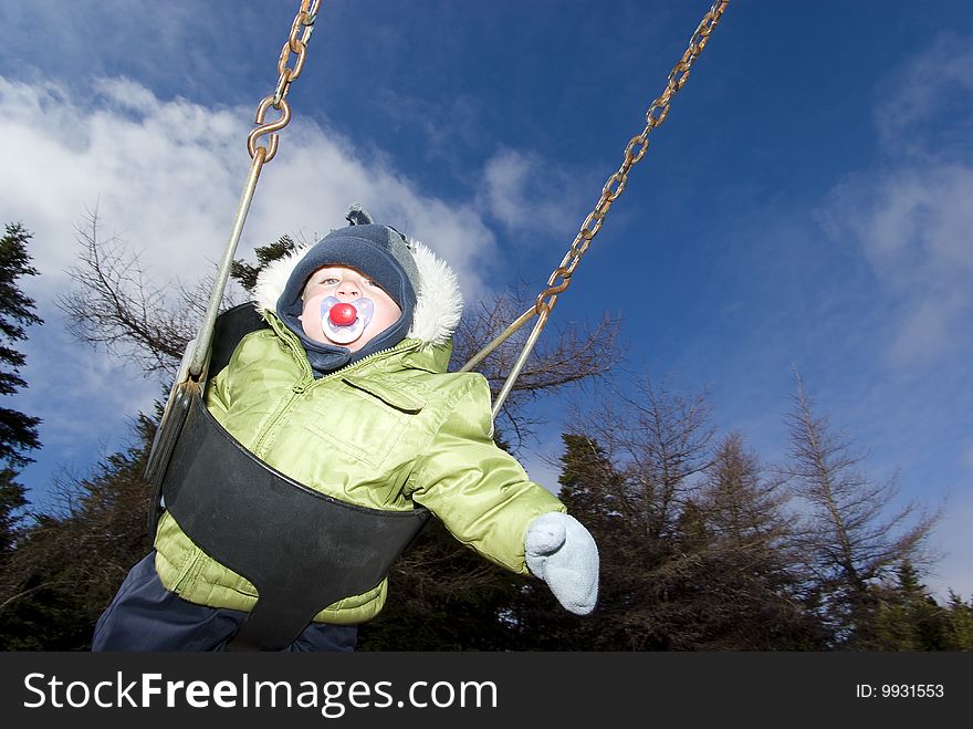 Baby swinging on playground during cold spring day