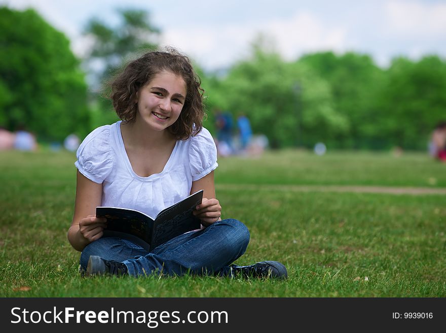 The girl with the open book sits on a grass and smiles. The girl with the open book sits on a grass and smiles