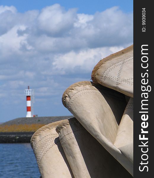 a detail of folded canvas of a sailing boat with a red/white striped lighthouse in the background. a detail of folded canvas of a sailing boat with a red/white striped lighthouse in the background