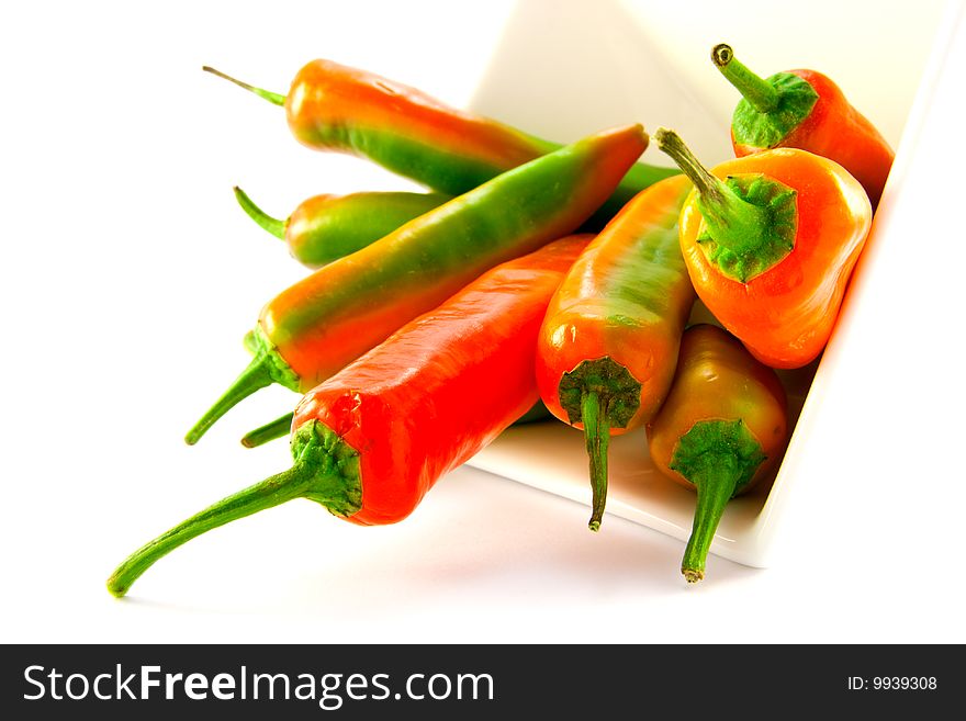 Red and green chillis spilling out of a white square bowl with clipping path on a white background. Red and green chillis spilling out of a white square bowl with clipping path on a white background