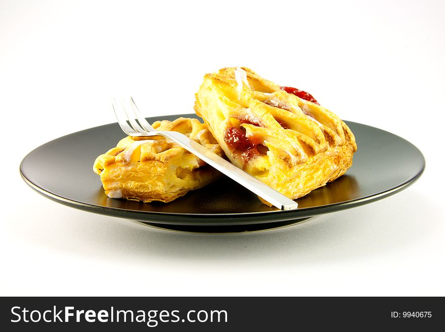 Raspberry and custard danish on a black plate with a fork on a white background. Raspberry and custard danish on a black plate with a fork on a white background