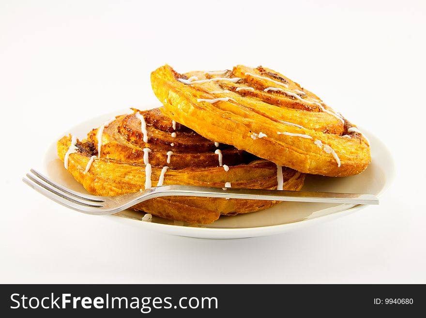 Two cinnamon buns on a plate with a fork with a clipping path on a white background. Two cinnamon buns on a plate with a fork with a clipping path on a white background