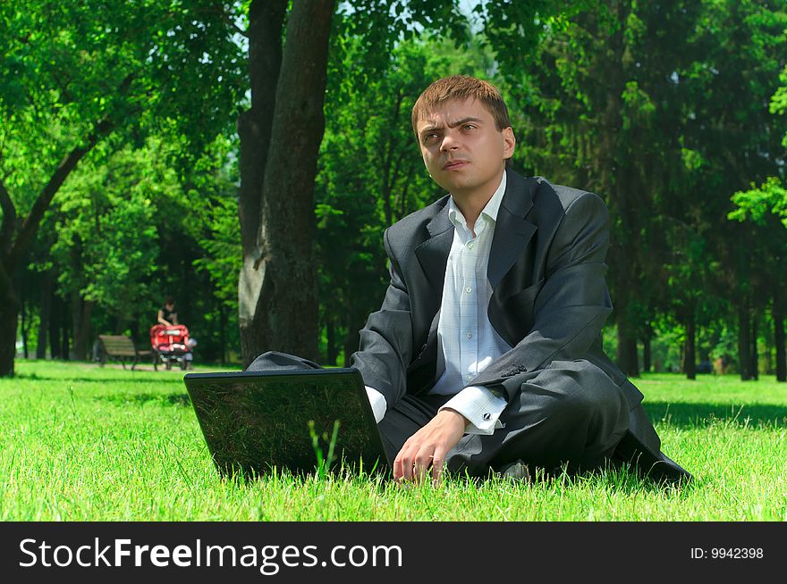 Young successful businessman resting in a park on the grass working on a laptop. Young successful businessman resting in a park on the grass working on a laptop