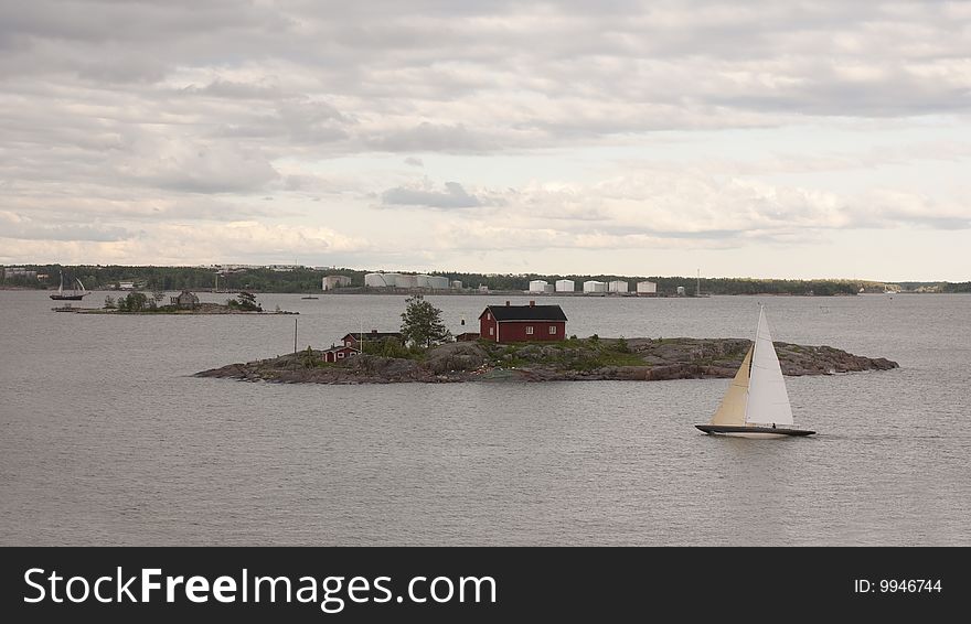 A view from the island of Luoto just across the bay from Helsinki, Finland. View is of a sailboat touring the area with a typical fisherman's cottage in the Baltic Sea in the Bay of Finland. A view from the island of Luoto just across the bay from Helsinki, Finland. View is of a sailboat touring the area with a typical fisherman's cottage in the Baltic Sea in the Bay of Finland.