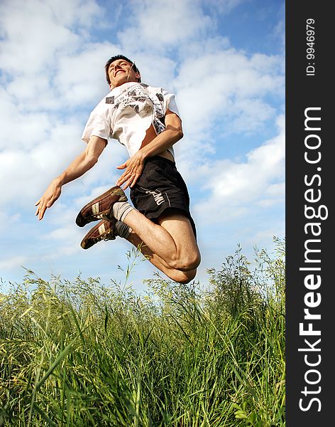Man jumping on a green meadow with a beautiful cloudy sky. Man jumping on a green meadow with a beautiful cloudy sky