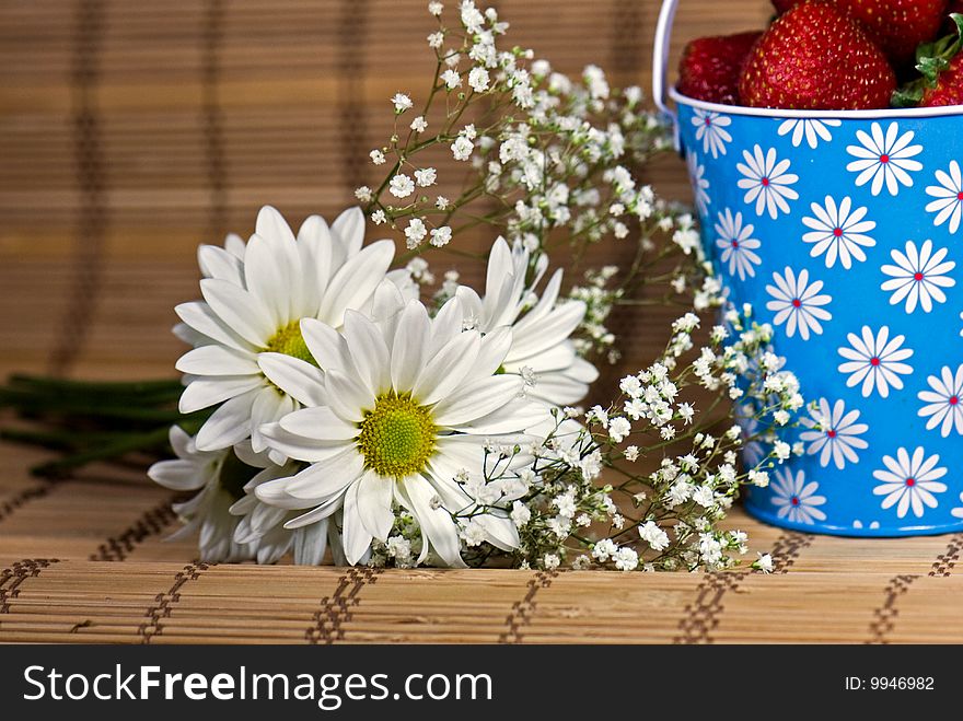 Daisies and a pail of strawberries on a bamboo mat. Daisies and a pail of strawberries on a bamboo mat.