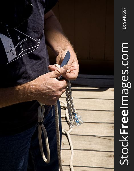 A sailor rigging, tying and cutting cables, in a classic wooden sailing ship, using a sailor’s hand knife. A sailor rigging, tying and cutting cables, in a classic wooden sailing ship, using a sailor’s hand knife