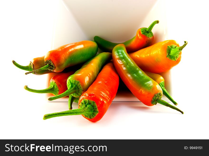 Red and green chillis spilling out of a white square bowl with clipping path on a white background. Red and green chillis spilling out of a white square bowl with clipping path on a white background