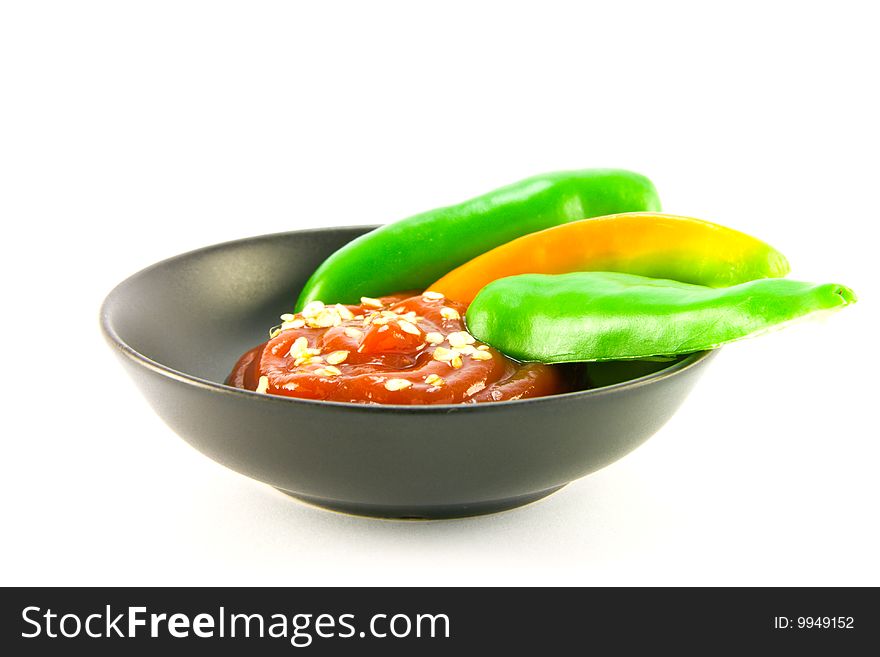 Whole chillis in a black bowl with red chilli dipping sauce with clipping path on a white background. Whole chillis in a black bowl with red chilli dipping sauce with clipping path on a white background