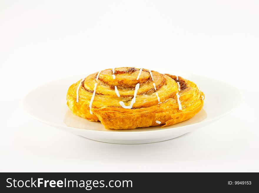 Single cinnamon bun on a plate with clipping path on a white background. Single cinnamon bun on a plate with clipping path on a white background