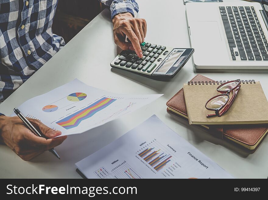 Business documents on office table with smartphone and tablet and graph financial and businessman working in the background