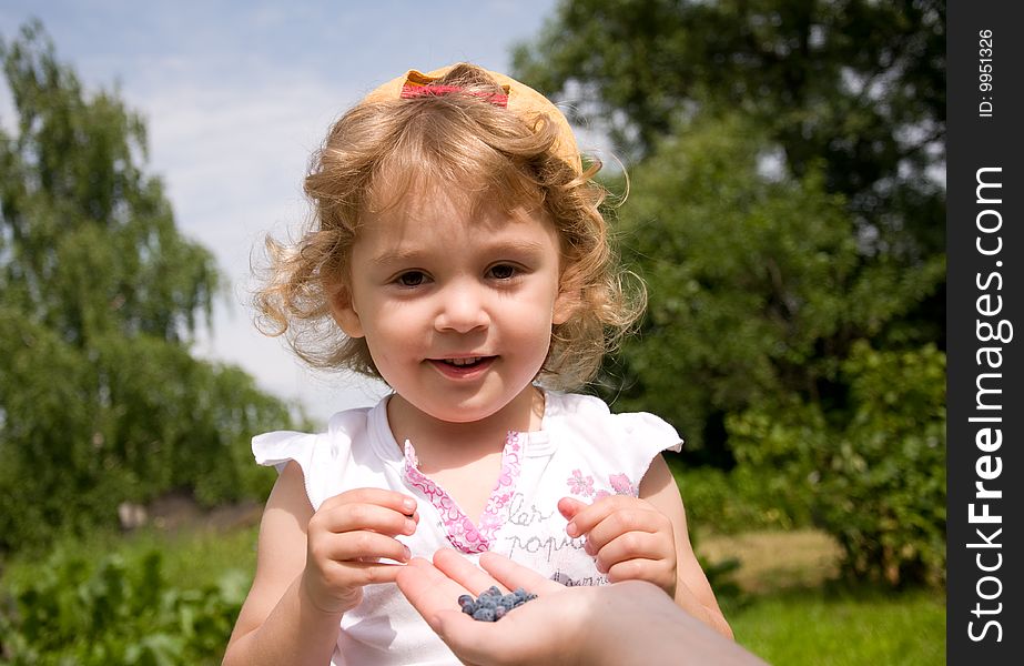 Beautiful little girl eating honeysuckle in the garden