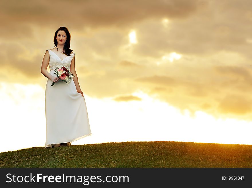 Young bride standing on a hill during sunset. Young bride standing on a hill during sunset.