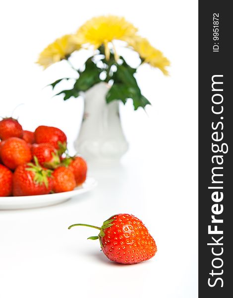 Fresh strawberry against a plate with berries and vases with the flowers. Fresh strawberry against a plate with berries and vases with the flowers