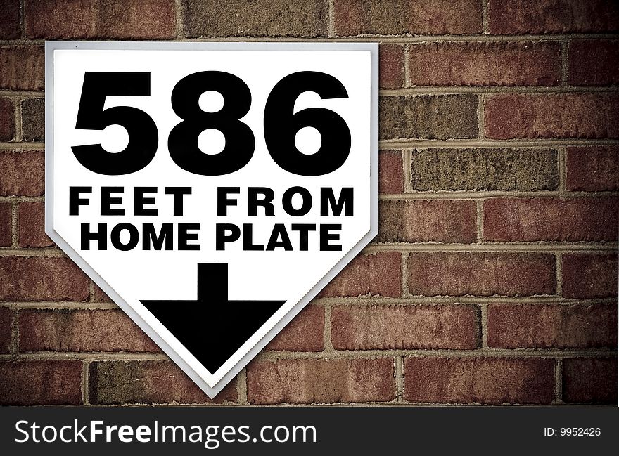 Stadium sign against a brick wall displaying distance to home plate with copy space.