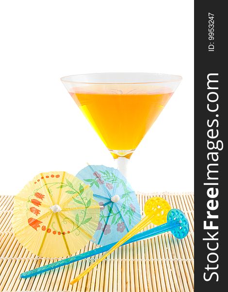 Orange cocktail on bamboo placemat with stearing sticks and small parasols on white