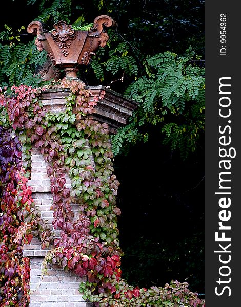 A brick pillar with vegetable mantle, holding an ancient earthenware vase. Ancient castle in Italy, Oltrepo Pavese, Montalto. A brick pillar with vegetable mantle, holding an ancient earthenware vase. Ancient castle in Italy, Oltrepo Pavese, Montalto.