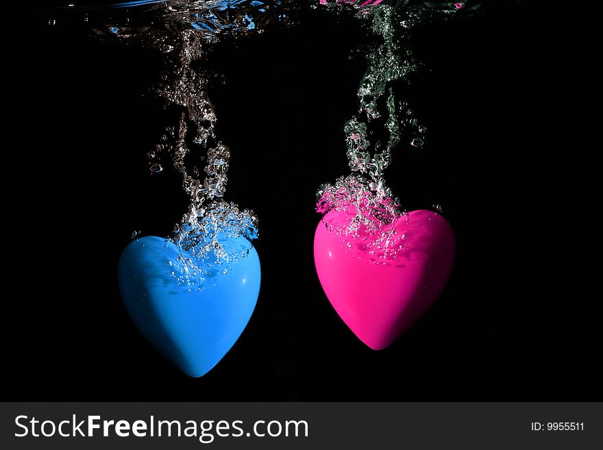 Pink and blue hearts splashing underwater against black background. Pink and blue hearts splashing underwater against black background