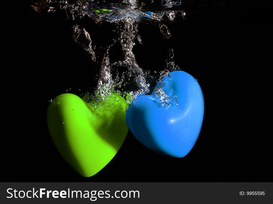 Green and blue Hearts splashing underwater against black background. Green and blue Hearts splashing underwater against black background
