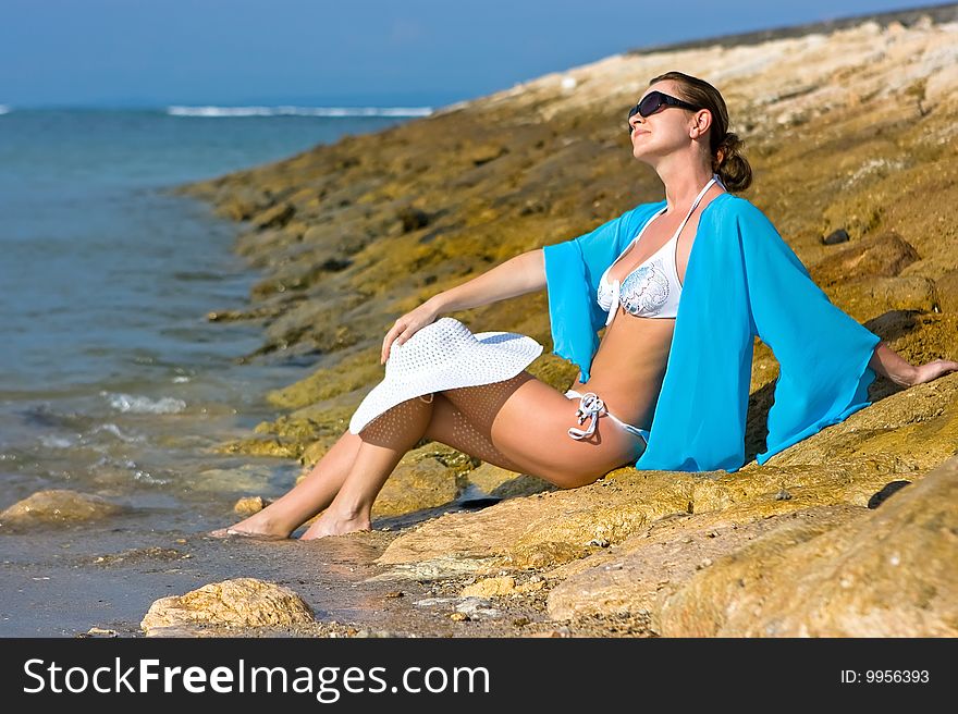 Brunette lady with white hat sitting on the rocky beach. Brunette lady with white hat sitting on the rocky beach