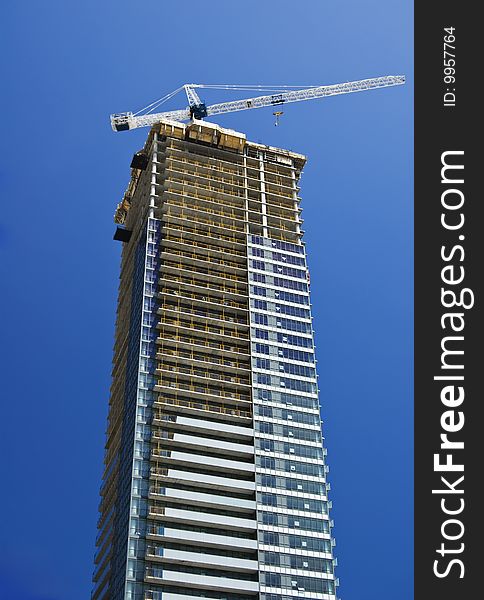 Modern glass and steel building under construction with a white crane on top against clear blue sky